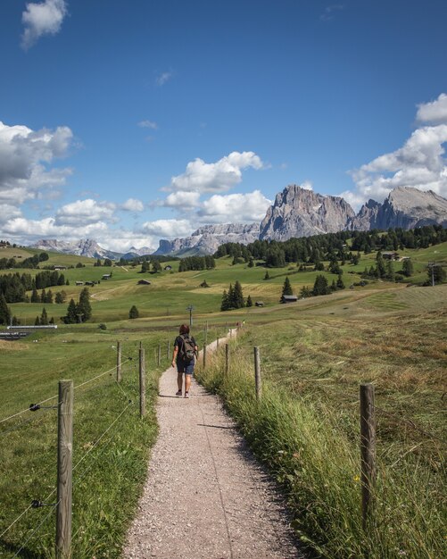 Foto vertical de uma pessoa caminhando em um caminho de terra com a montanha Plattkofel