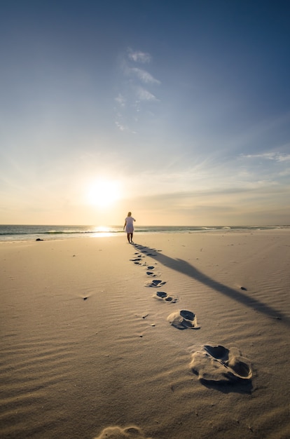 Foto vertical de uma pessoa caminhando na praia com passos em primeiro plano