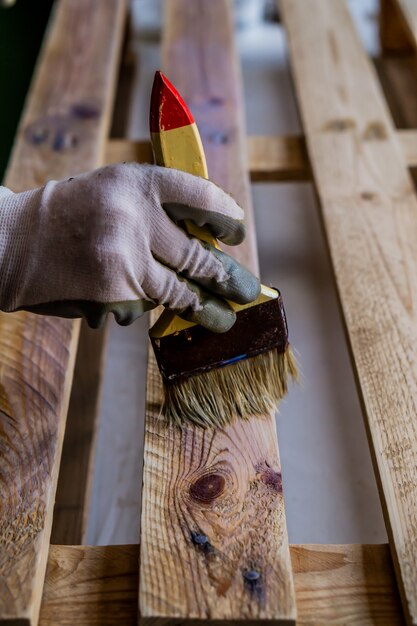 Foto vertical de uma pessoa pintando um palete de madeira com um pincel