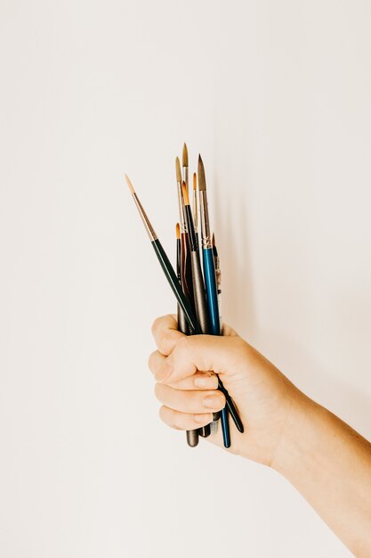 Foto vertical de uma pessoa segurando um punhado de pincéis de pintura