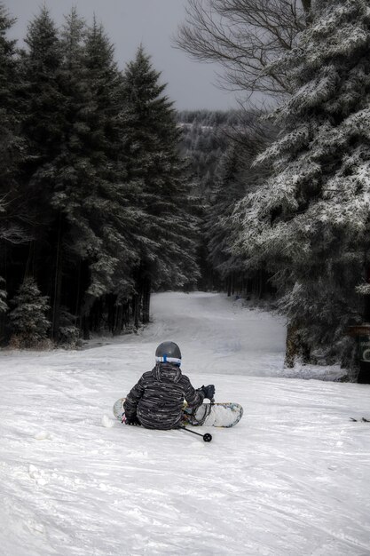 Foto vertical de uma pessoa sentada na colina usando uma prancha de snowboard