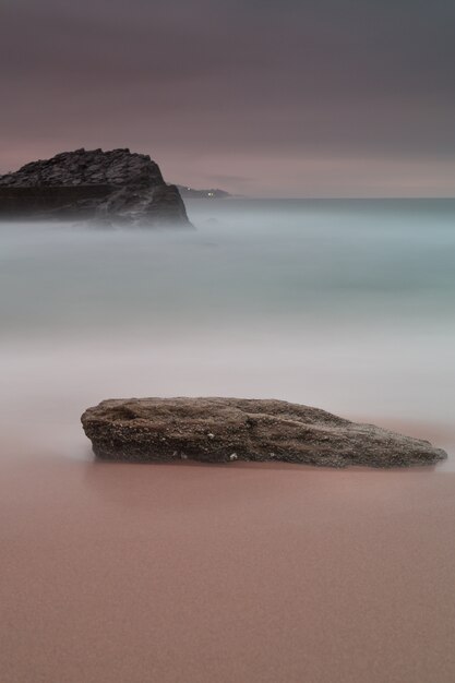 Foto vertical de uma rocha na costa sob o céu roxo escuro