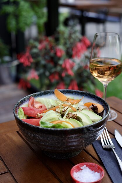 Foto vertical de uma salada vegetariana com abacate, tomate e nozes em uma mesa com uma bebida