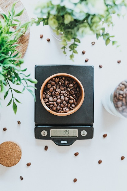 Foto vertical de uma tigela cheia de grãos de café em escala digital preta de 39 gramas