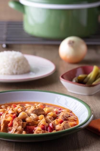 Foto vertical de uma tigela de sopa de legumes, uma tigela de picles e um prato de arroz em uma mesa de madeira