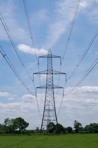 Foto vertical de uma torre de transmissão de energia elétrica suspensa em um campo sob o céu