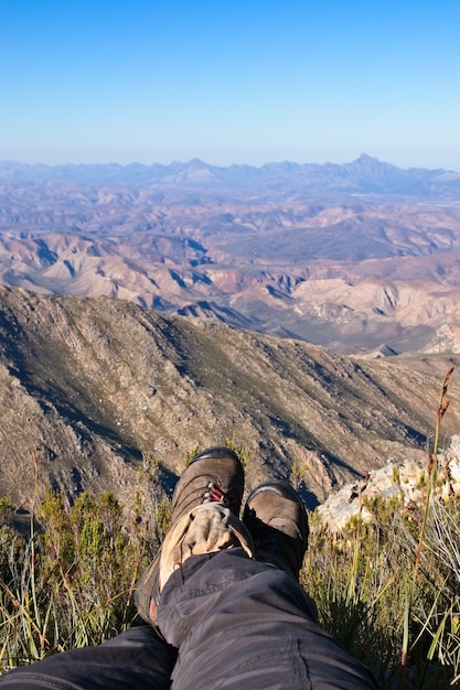 Foto vertical dos pés de uma pessoa sentada no topo de uma colina em um belo vale