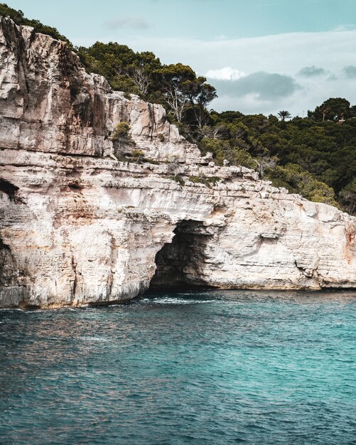 Foto vertical incrível de uma caverna localizada na enorme rocha e na costa do mar