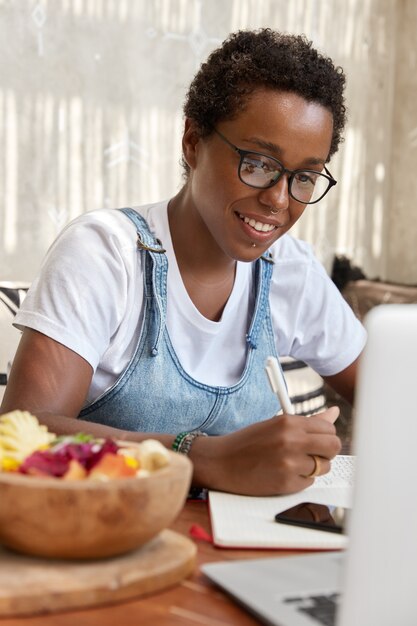 Foto vertical interna de uma alegre jovem negra afro-americana olhando positivamente para o monitor