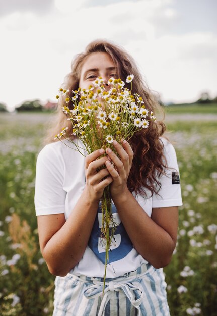 Foto vertical superficial de um modelo encaracolado segurando um buquê de margaridas