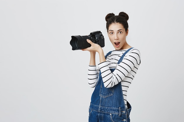 Fotógrafa criativa e animada tirando fotos para a câmera, parecendo divertida enquanto fotografa