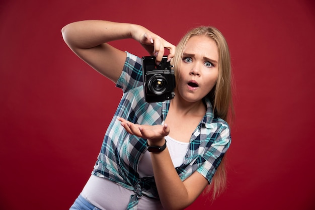 Fotografia de jovem loira segurando uma câmera profissional e não sabe como usá-la.