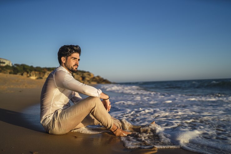 Foto grátis fotografia de um homem moreno sentado na areia em uma praia