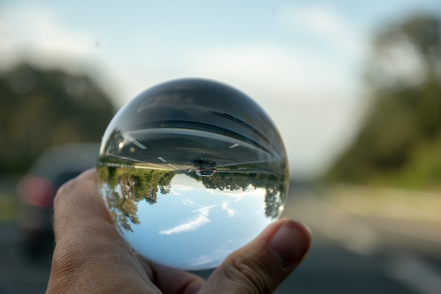 Fotografia em close-up de uma pessoa segurando uma bola de cristal com o reflexo de árvores