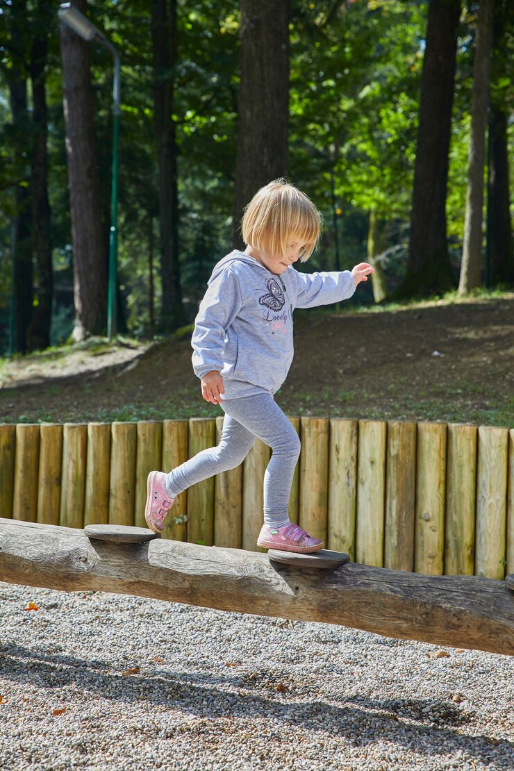 Foto grátis fotografia vertical de uma menina caminhando em um tubo de madeira no playground