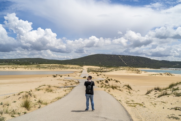 Fotógrafo do sexo masculino caminhando por uma praia sob um céu nublado durante o dia na Andaluzia, Espanha