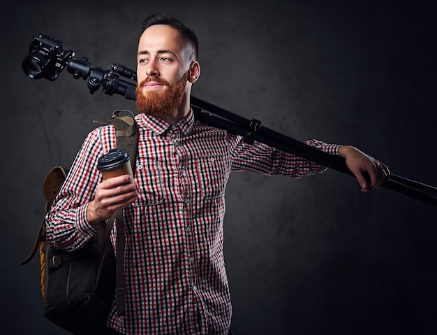 Fotógrafo freelance barbudo ruivo com tripé e mochila.