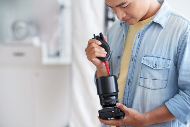 Fotógrafo masculino asiático, limpeza de lente da câmera com ventilador de ar