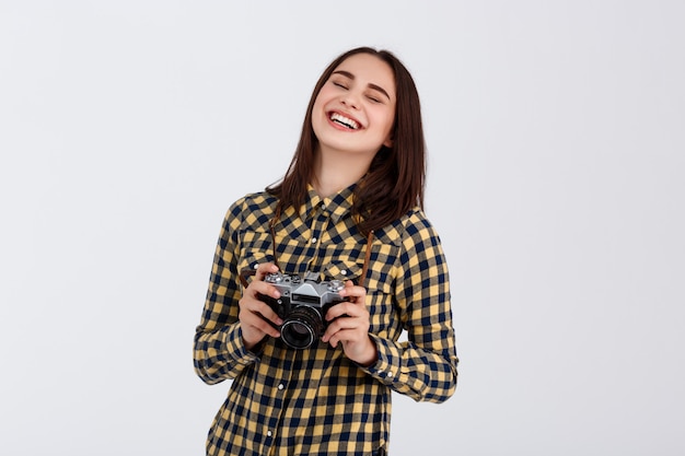 Fotógrafo moreno de sorriso bonito novo sobre a parede branca.