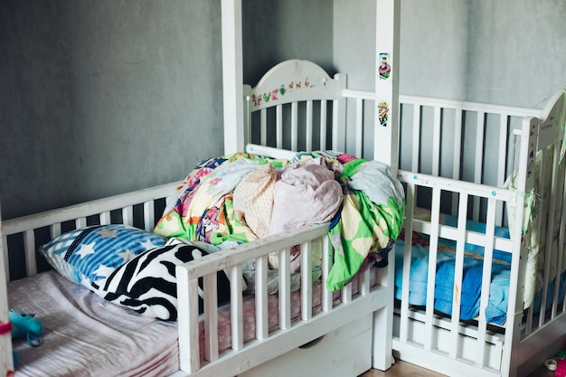 Fragmento de foto de quarto de criança com coisas espalhadas, travesseiros e colchas nas camas