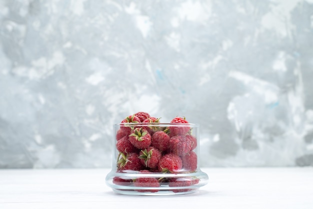 Framboesas vermelhas frescas dentro de uma tigela transparente em branco