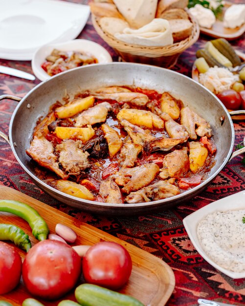 Frango e batatas grelhadas em molho oleoso em uma panela, legumes ao redor.