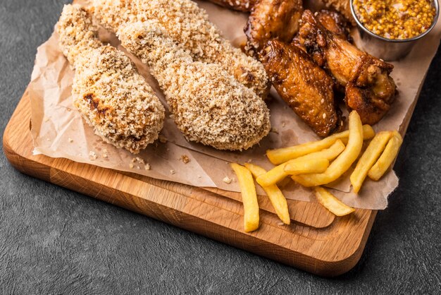 Frango frito em ângulo alto na tábua de cortar com batatas fritas