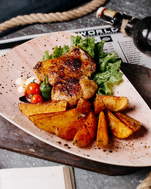 Frango frito servido com batatas, tomate cereja, pimenta e alface