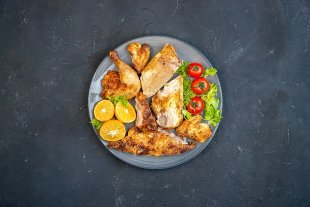 Frango frito, tomates, fatias de limão em um prato oval no espaço livre de vista de cima