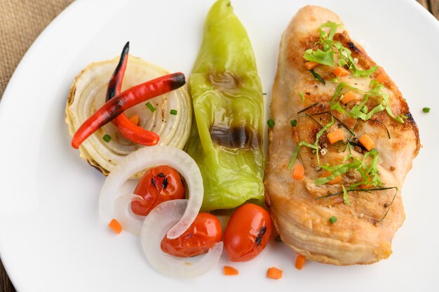 Frango grelhado em um prato branco com tomate, salada, cebola, pimenta e molho.