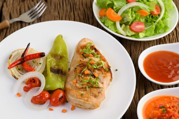 Frango grelhado em um prato branco com tomate, salada, cebola, pimenta e molho.