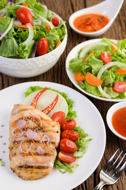 Frango grelhado em um prato branco com tomate, salada, cebola, pimenta e molho.