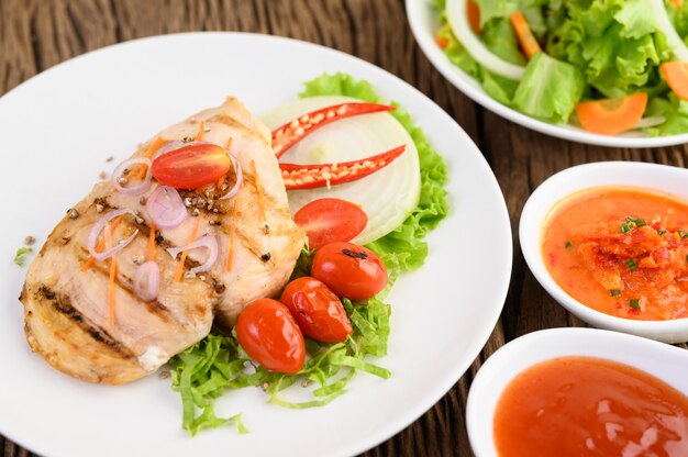 Frango grelhado em um prato branco com tomate, salada, cebola, pimenta e molho.