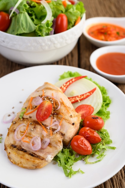 Frango grelhado em um prato branco com tomate, salada, cebola, pimenta e molho.