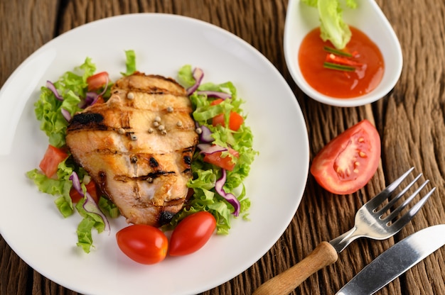 Frango grelhado em um prato branco com uma salada de tomate, cenoura e pimentão cortado em pedaços.