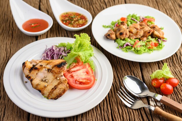 Frango grelhado em um prato branco com uma salada de tomate, cenoura e pimentão cortado em pedaços.