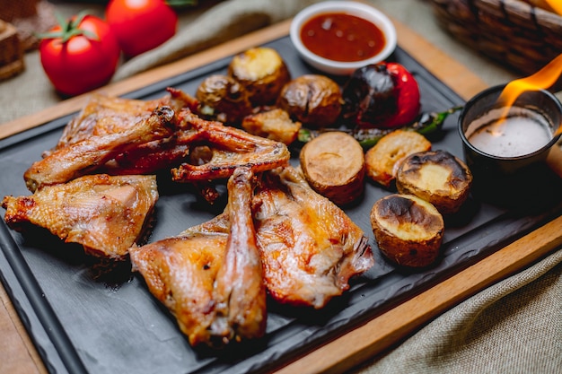 Frango grelhado na tábua de madeira batata tomate tomate molho de pimenta vista lateral