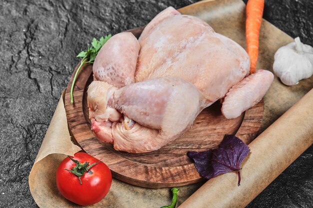 Frango inteiro cru no prato de madeira com legumes frescos