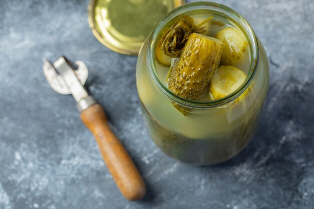 Frasco aberto cheio de pepino em conserva em fundo cinza