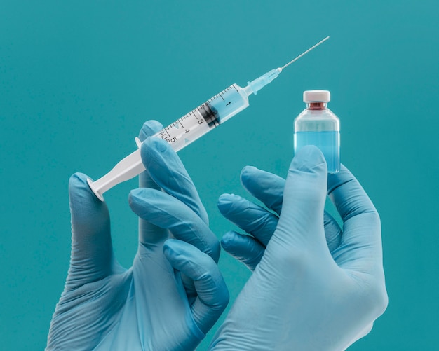 Frasco de vacina e seringa segurados por médico com luvas
