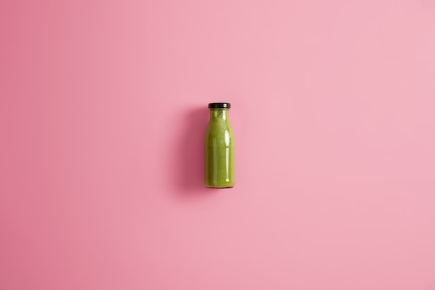 Frasco de vidro de batido refrescante feito de espinafre, pepino e abacate, com poucas calorias, isolado no fundo rosa. Conceito de dieta e estilo de vida saudável. Vegetais verdes misturados para beber