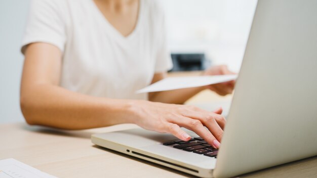 Freelance jovem empresária da Ásia casual wear usando laptop, trabalhando na sala de estar em casa.