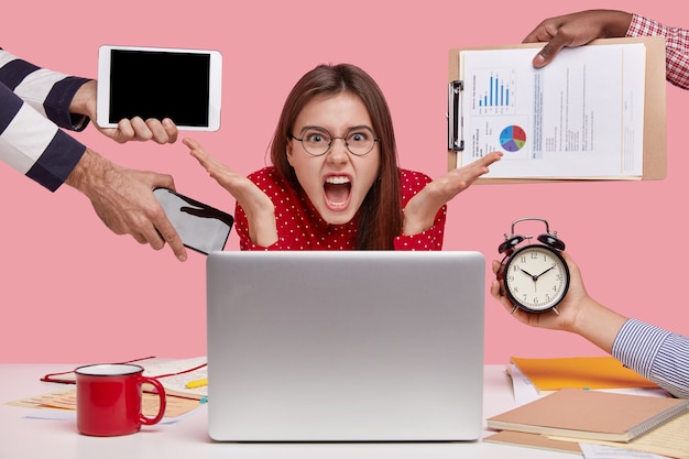 Foto grátis freelancer aborrecido gesticula em frente ao laptop, tem muita papelada, faz hora extra, chora desesperadamente