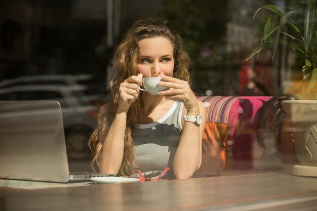 Freelancer bebendo uma xícara de café quente no terraço de verão Garota de cabelo comprido esperando um cliente