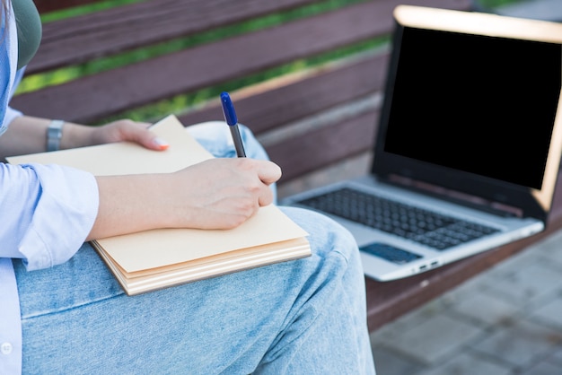 Freelancer de garota caucasiana, sentado em um banco e escrevendo em um caderno. conceito de educação e jornalismo
