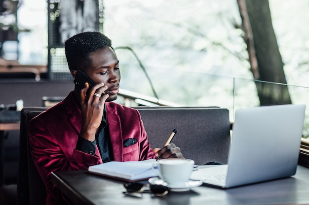 Freelancer masculino bem sucedido, falando por telefone, empresário pensativo trabalhar na netbook no terraço caffee.