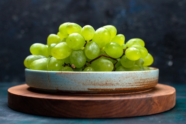 Frente close vista uvas verdes frescas frutas maduras e suculentas dentro do prato na mesa azul escuro.