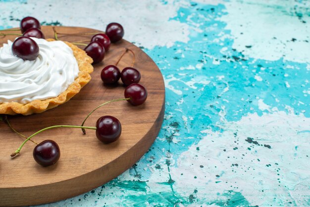 Frente fechar bolo cremoso com cerejas frescas isoladas em mesa azul claro, bolo de cor de bolo de biscoito creme
