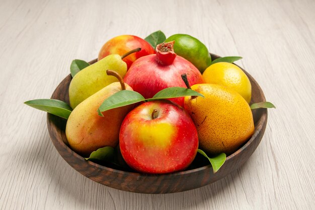 Frente frutas frescas maçãs pêras e outras frutas dentro do prato na mesa branca frutas maduras árvore maduras muitas frescas