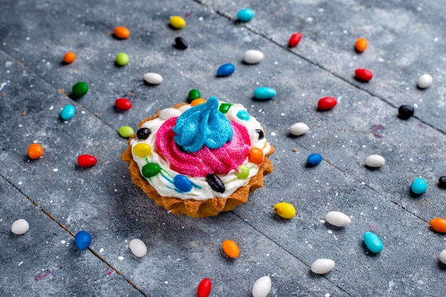 Frente mais de perto, um pequeno bolo gostoso com creme e vários doces coloridos, tudo aceso